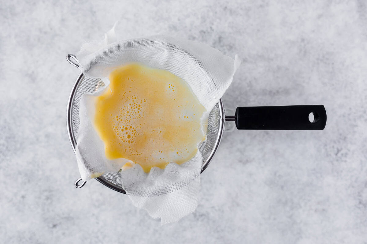 Pineapple water being strained through a cheesecloth lines sieve.