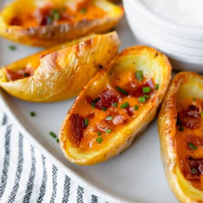 Close up of crispy loaded potato skins on a plate with a striped linen underneath.
