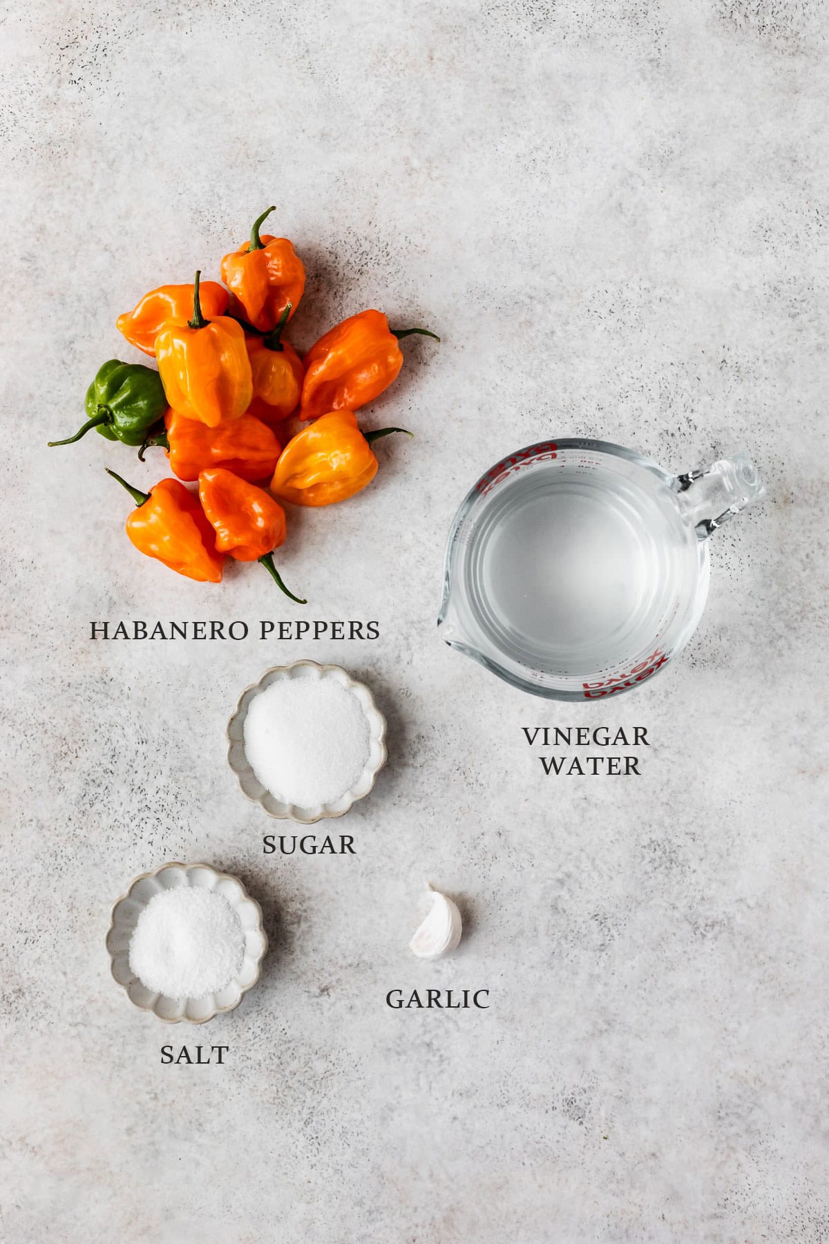 Ingredients needed to make pickled habanero peppers on a gray background with text overlay.