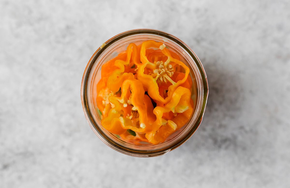 Thinly sliced habanero peppers in a glass jar.