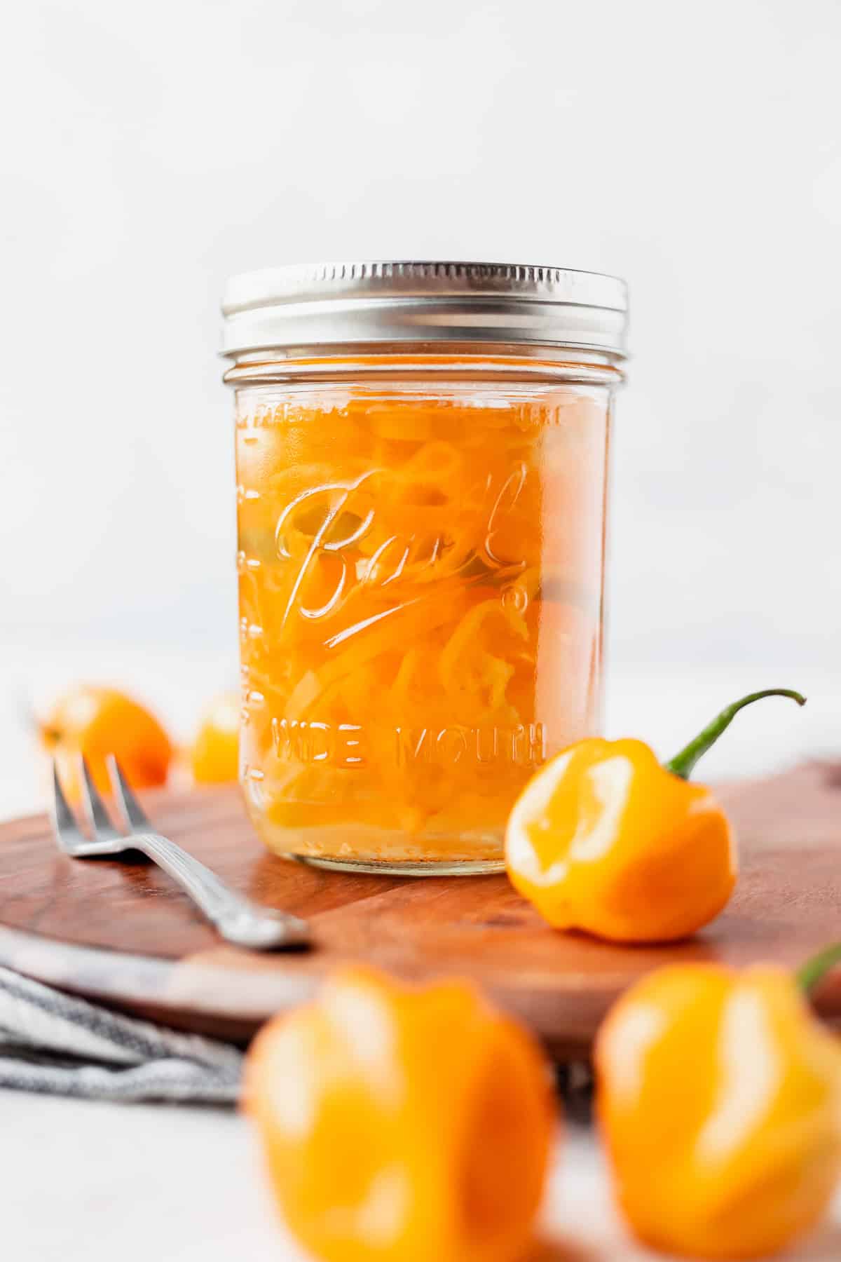A jar of pickled habanero peppers with more peppers and a fork around it.