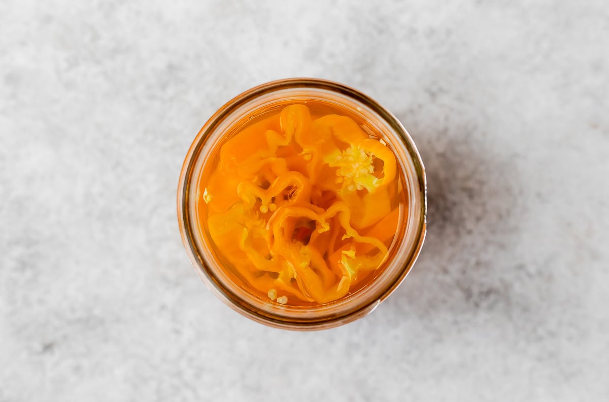 Overhead view of sliced habanero peppers in a glass jar with pickling liquid.