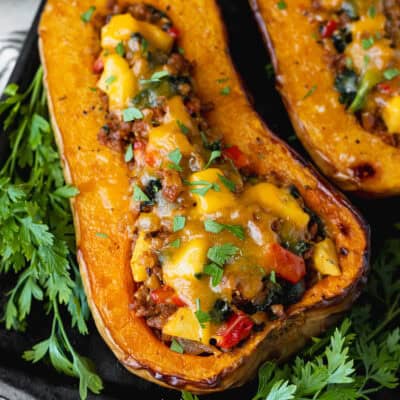 Close up of a sausage apple stuffed butternut squash with parsley around it.