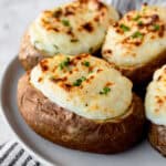 Close up of 3 sour cream and chive twice baked potatoes on a white plate.