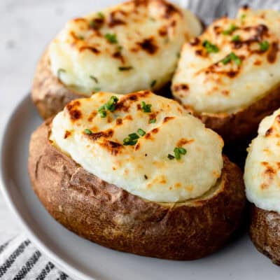 Close up of 3 sour cream and chive twice baked potatoes on a white plate.