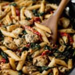 Close up of Tuscan Chicken Pasta in a black skillet with a wood server in it.