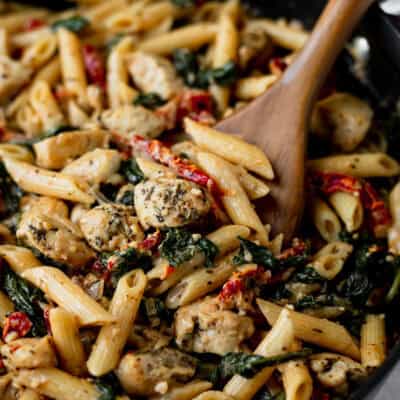 Close up of Tuscan Chicken Pasta in a black skillet with a wood server in it.