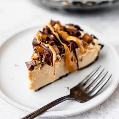 A slice of peanut butter pie with chopped Reese's cups and chocolate and peanut butter drizzle all over the top.