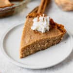 A slice of rutabaga pie topped with whipped cream and cinnamon on a white plate with cinnamon sticks in the background.