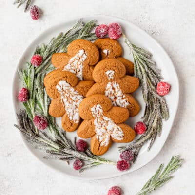 A white plate with gingerbread cookies surrounded by sugared rosemary and cranberries with more rosemary and cranberries around it.