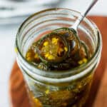 Close up of candied jalapeno peppers being lifted up with a fork from a mason jar.