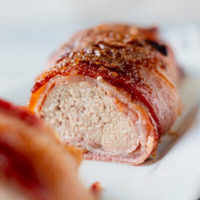 Close up of bacon wrapped pork tenderloin with a brown sugar and honey glaze cut in half.