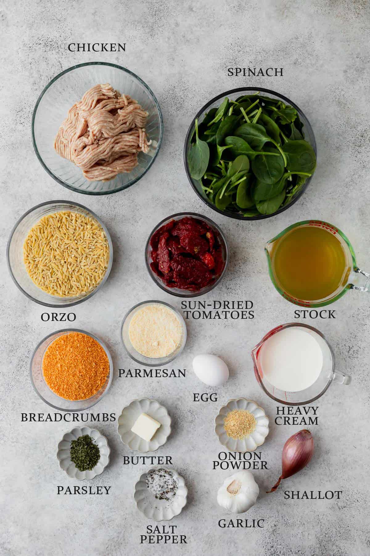 Ingredients needed to make Tuscan Chicken Meatballs with Orzo on a light gray background with text overlay that reads "chicken, spinach, orzo, sun-dried tomatoes, stock, heavy cream, parmesan, breadcrumbs, oregano, salt, pepper, garlic, shallot, onion powder, egg."