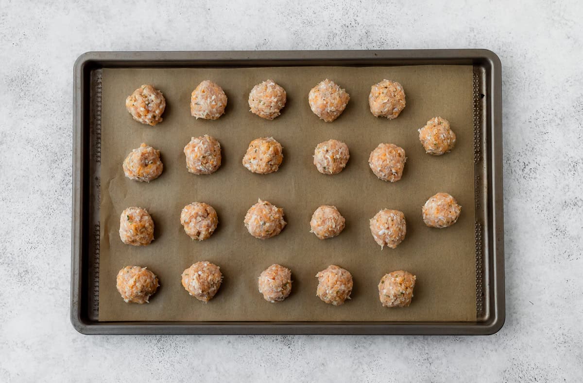 unbaked chicken meatballs on a parchment paper-lined baking sheet.