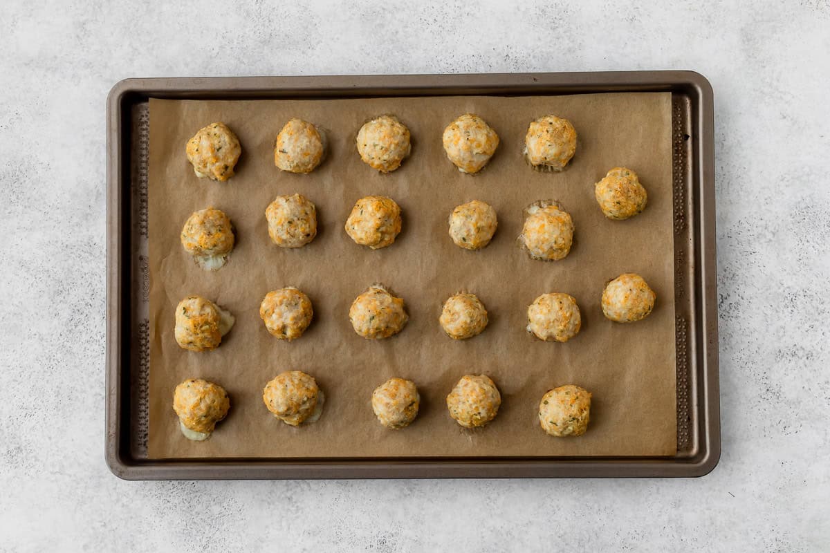 20 baked chicken meatballs on a parchment-paper lined baking sheet.