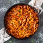 Overhead view of Creamy Cajun Chicken Pasta with peppers and onions in a black skillet over a light linen and a dark green background.