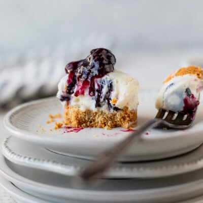 A mini blueberry cheesecake on a stack of small plates with a bite taken out on a fork next to it on the plate. There is a striped linen around it.