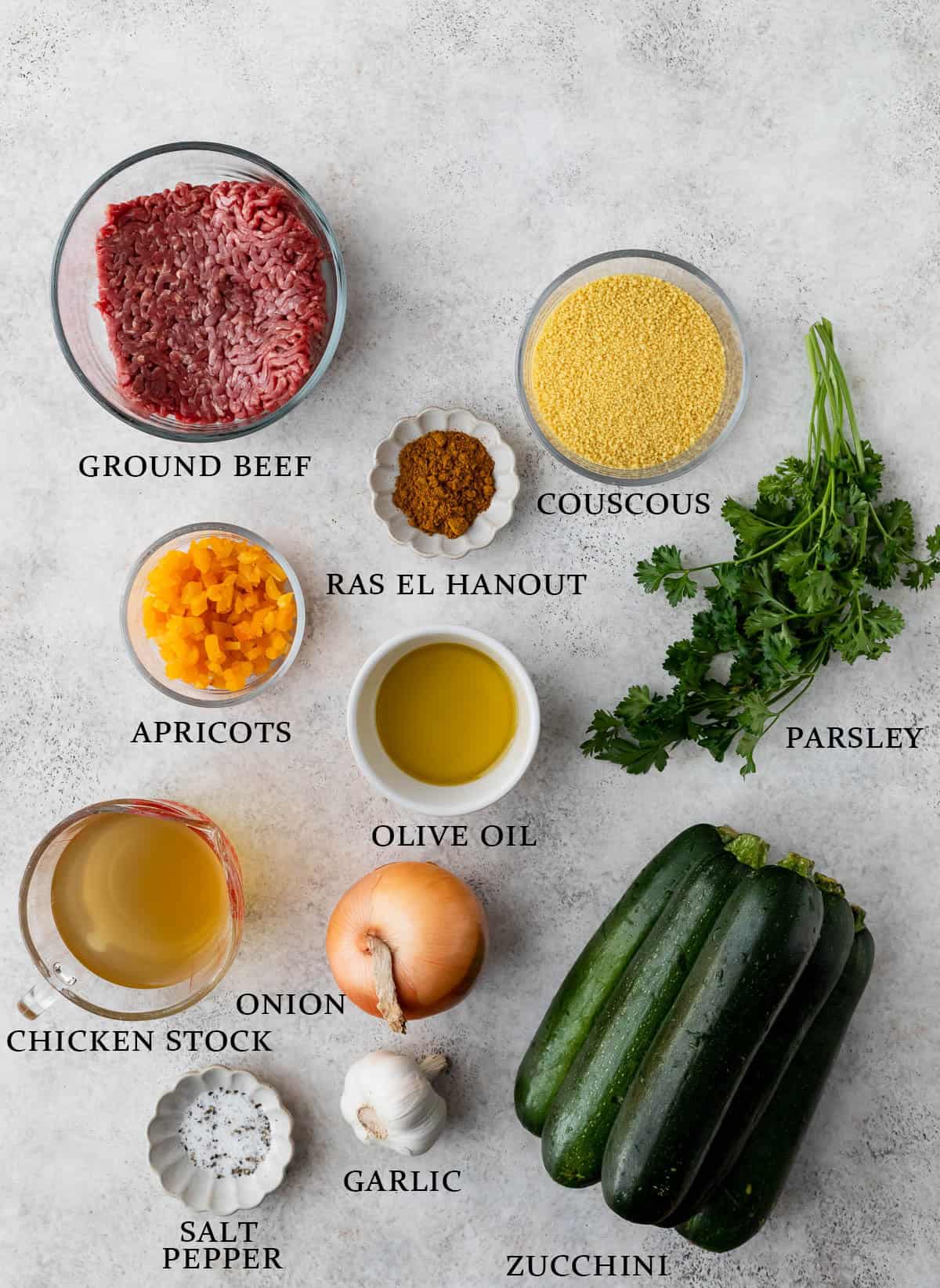 Ingredients need to make stuffed zucchini with text overlay that reads "beef, apricots, couscous, parsley, zucchini, onion, garlic, salt, pepper, chicken stock, ras el hanout."