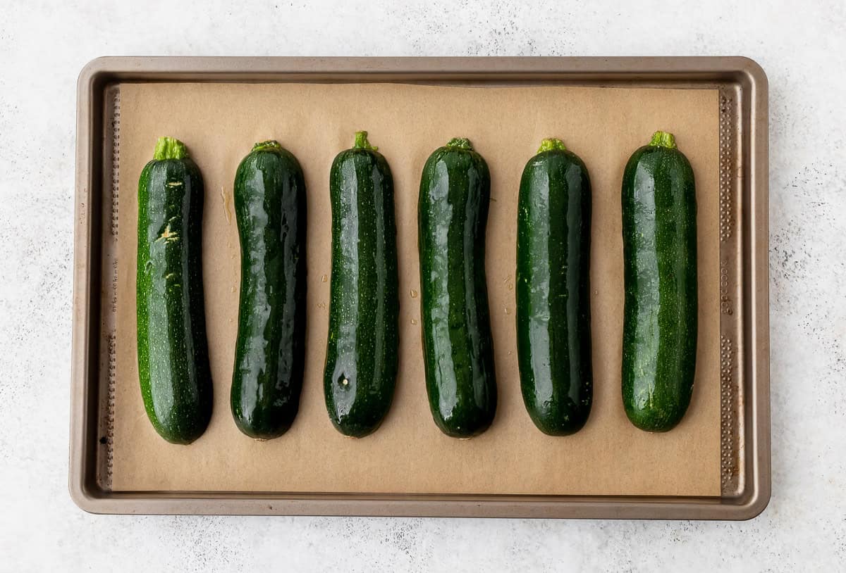 6 zucchini halves cut side down on a parchment paper lined baking sheet.