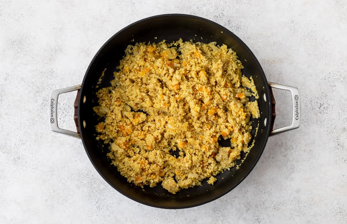 Couscous, apricots and onions cooking in a large, black skillet.