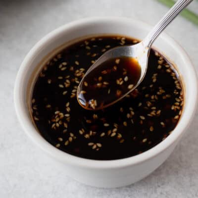 Close up of a white bowl filled with homemade teriyaki sauce with a small spoon lifting some up.
