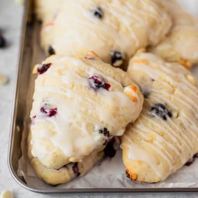 Close up of a stack of white chocolate blueberry scones on a parchment paper lined tray with white chocolate chips and blueberries around it.