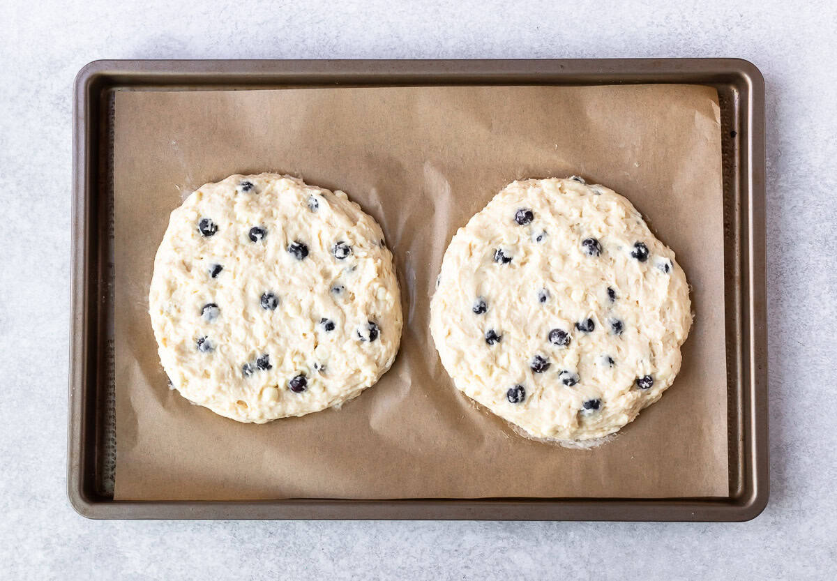 2 rounds of white chocolate chip blueberry scones dough on a parchment paper lined baking sheet.