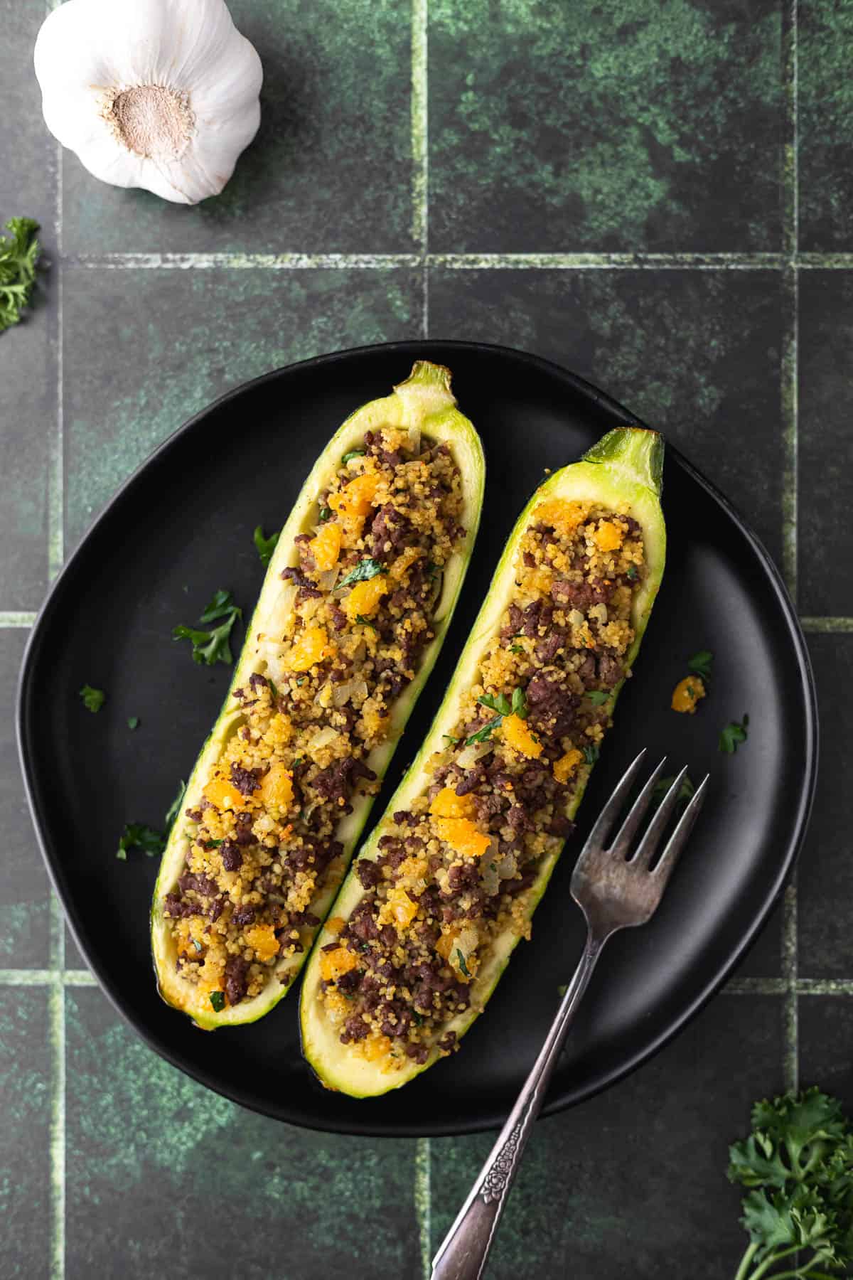Overhead of 2 Moroccan stuffed zucchini halves on a black plate over a dark green background.