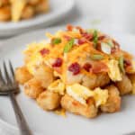 A pile of Breakfast Totchos on a white plate with a fork and a second plate partially showing in the background.