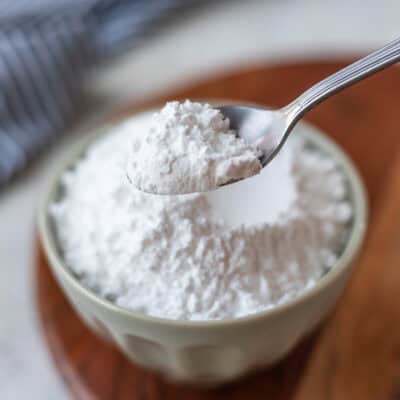 Homemade powdered sugar on a small spoon held up over a small bowl of powdered sugar.