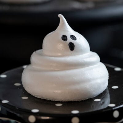 A single ghost marshmallow on a black and white stand with a black background.