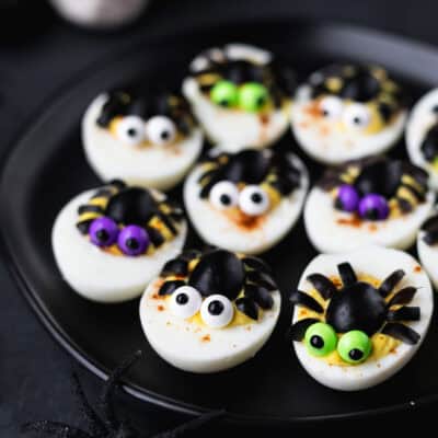 9 spider deviled eggs on a black plate over a black background.